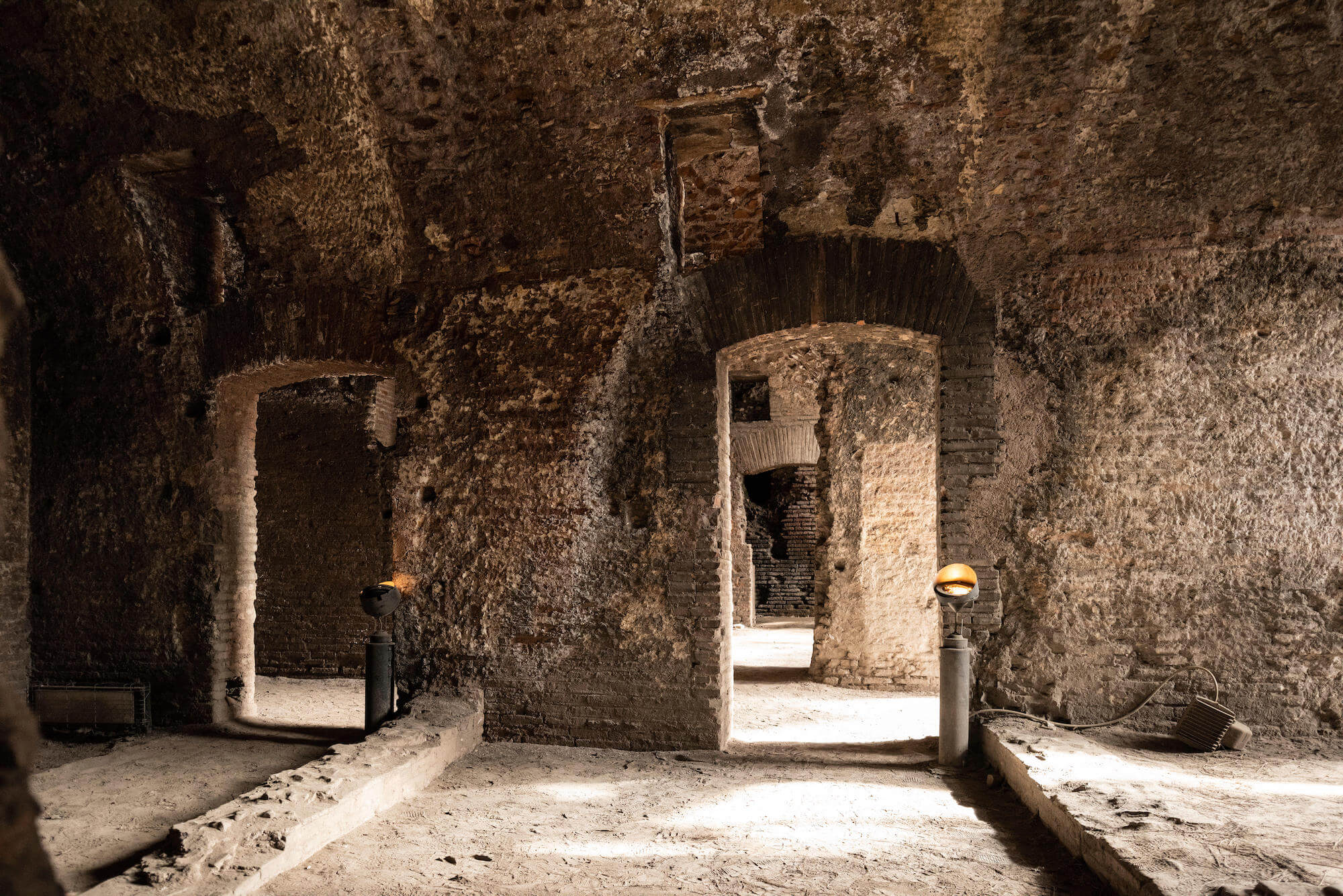 Inside a room. The walls are made of brick and it is quite dark. There are low walls where the room would have been divided into smaller spaces.