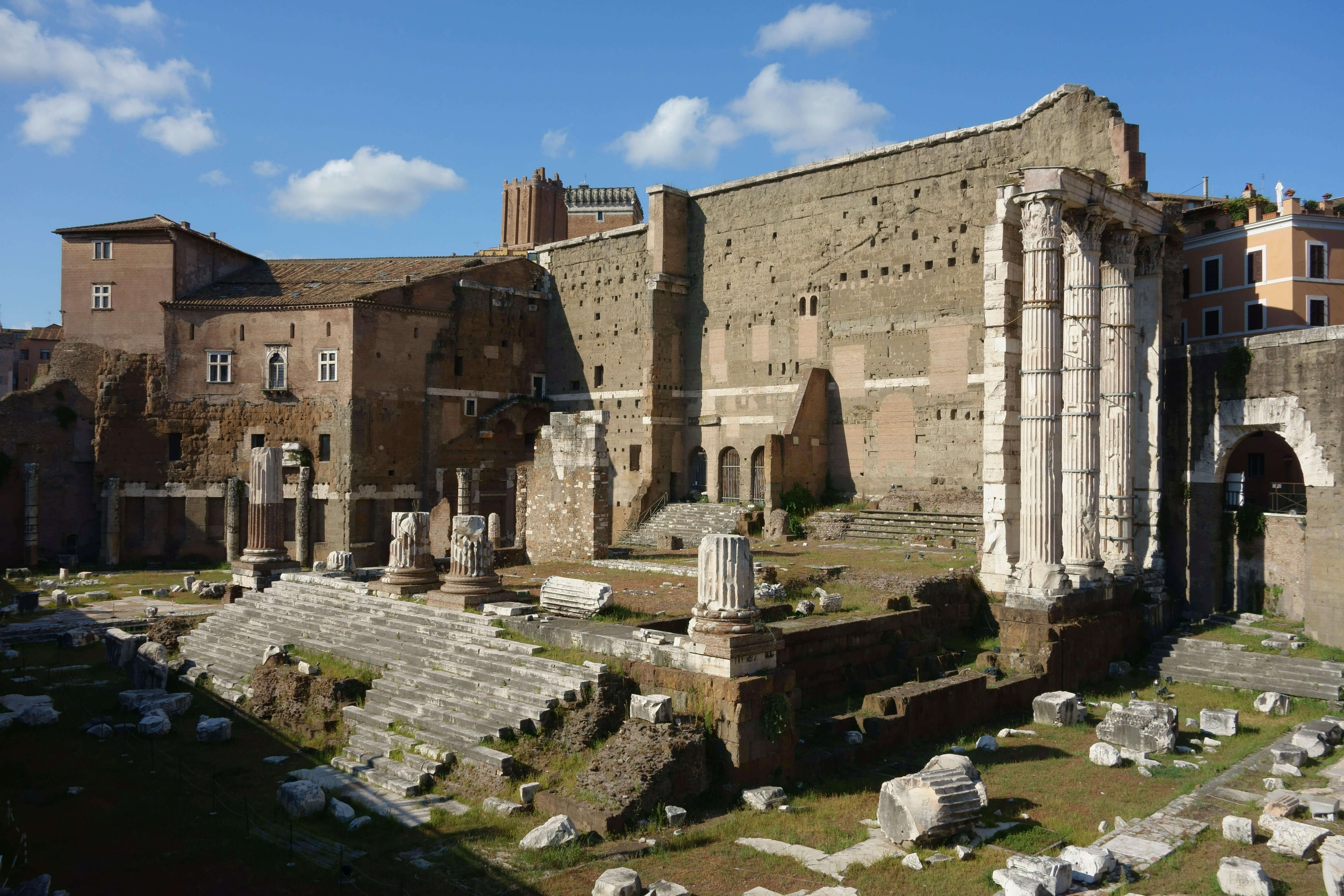 The remains of the Forum Augustus. A few columns are still standing in the foreground and a big wall towers behind.